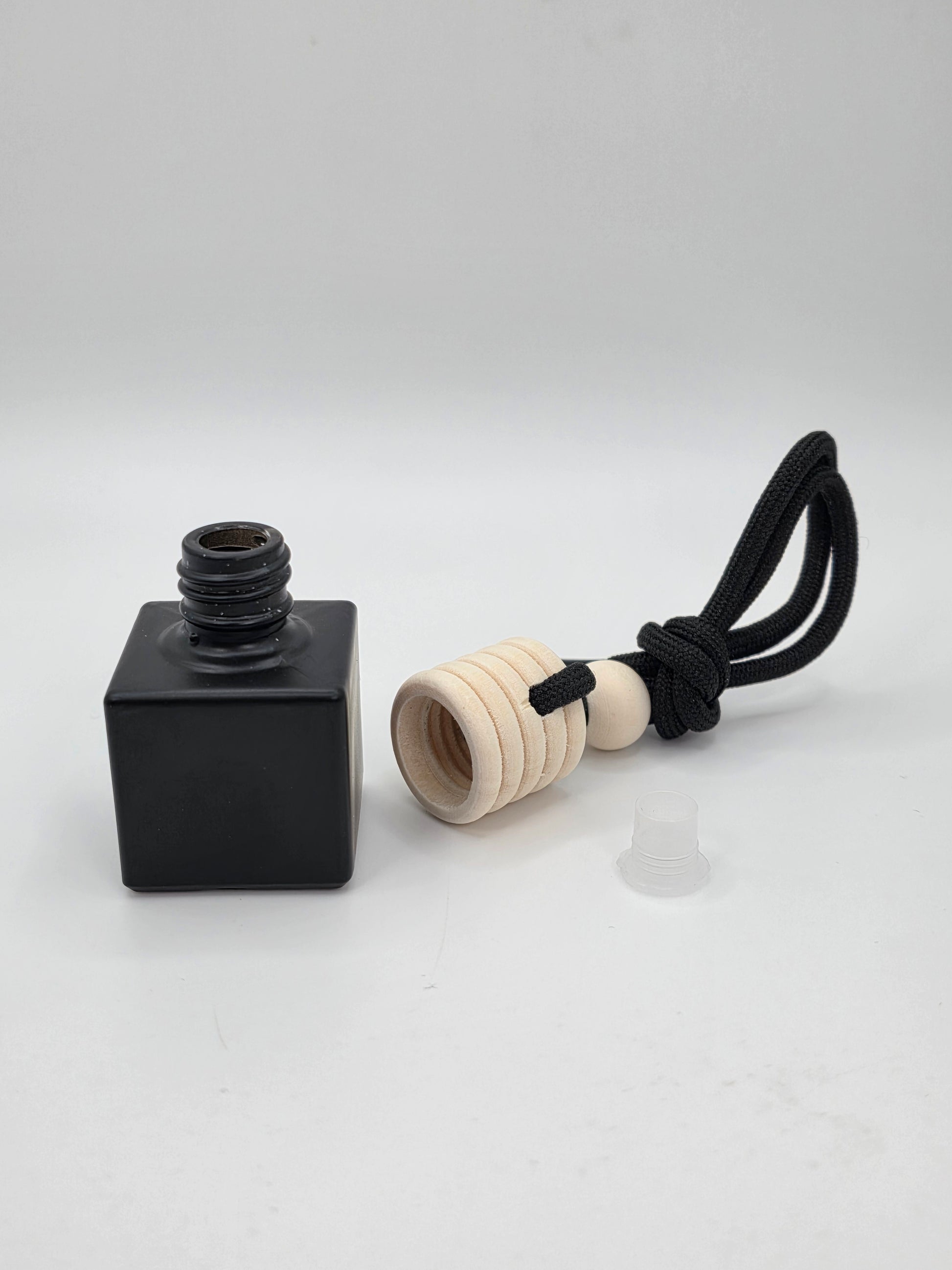 Imperial Undeniable Car Air Freshener – Open black glass bottle with wooden cap, plastic stopper, and black hanging cord displayed separately