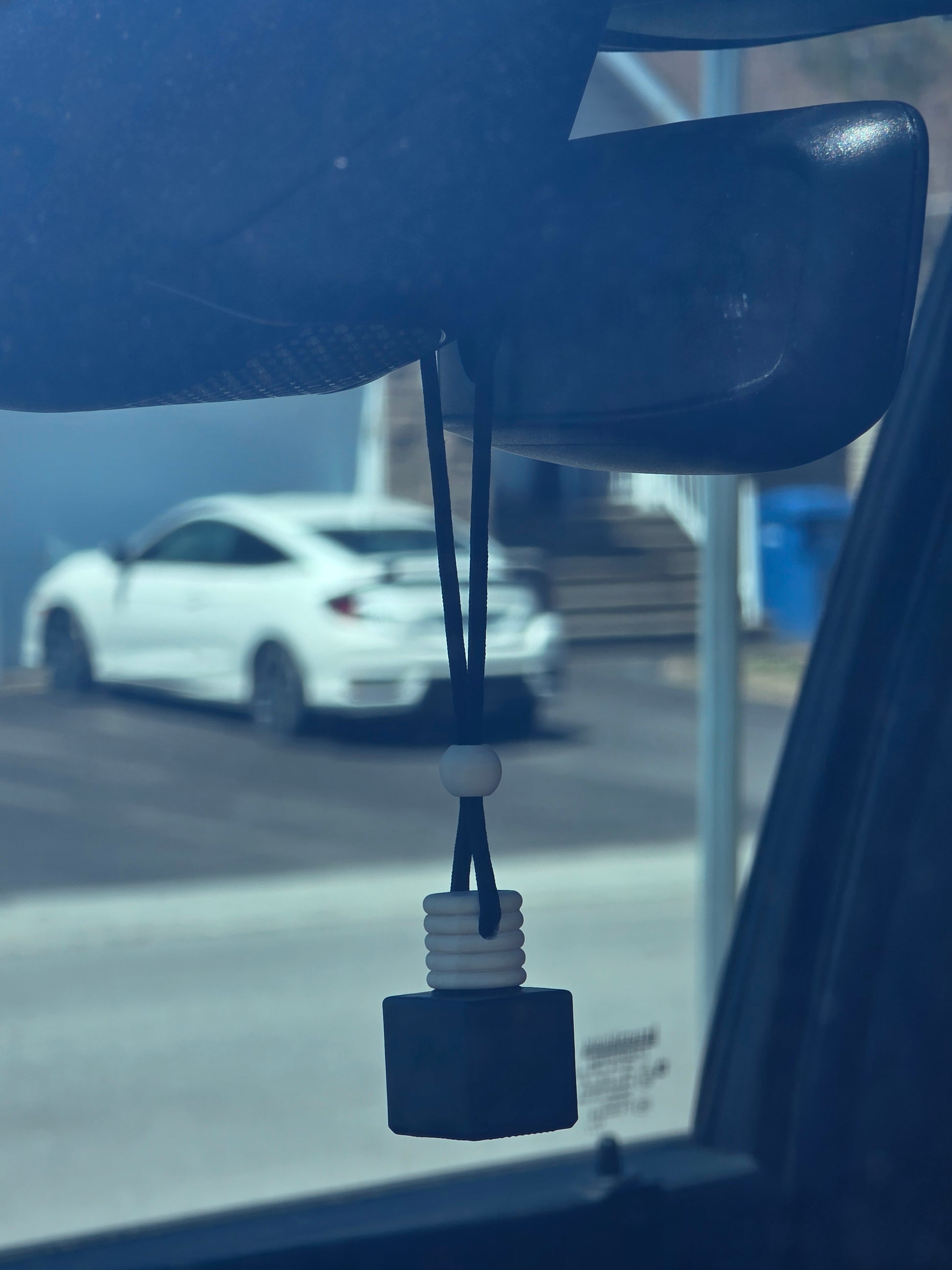 Imperial Ancient Imperial Oud Car Air Freshener – Square black bottle with wooden cap, hanging from rearview mirror inside a car with suburban street in background